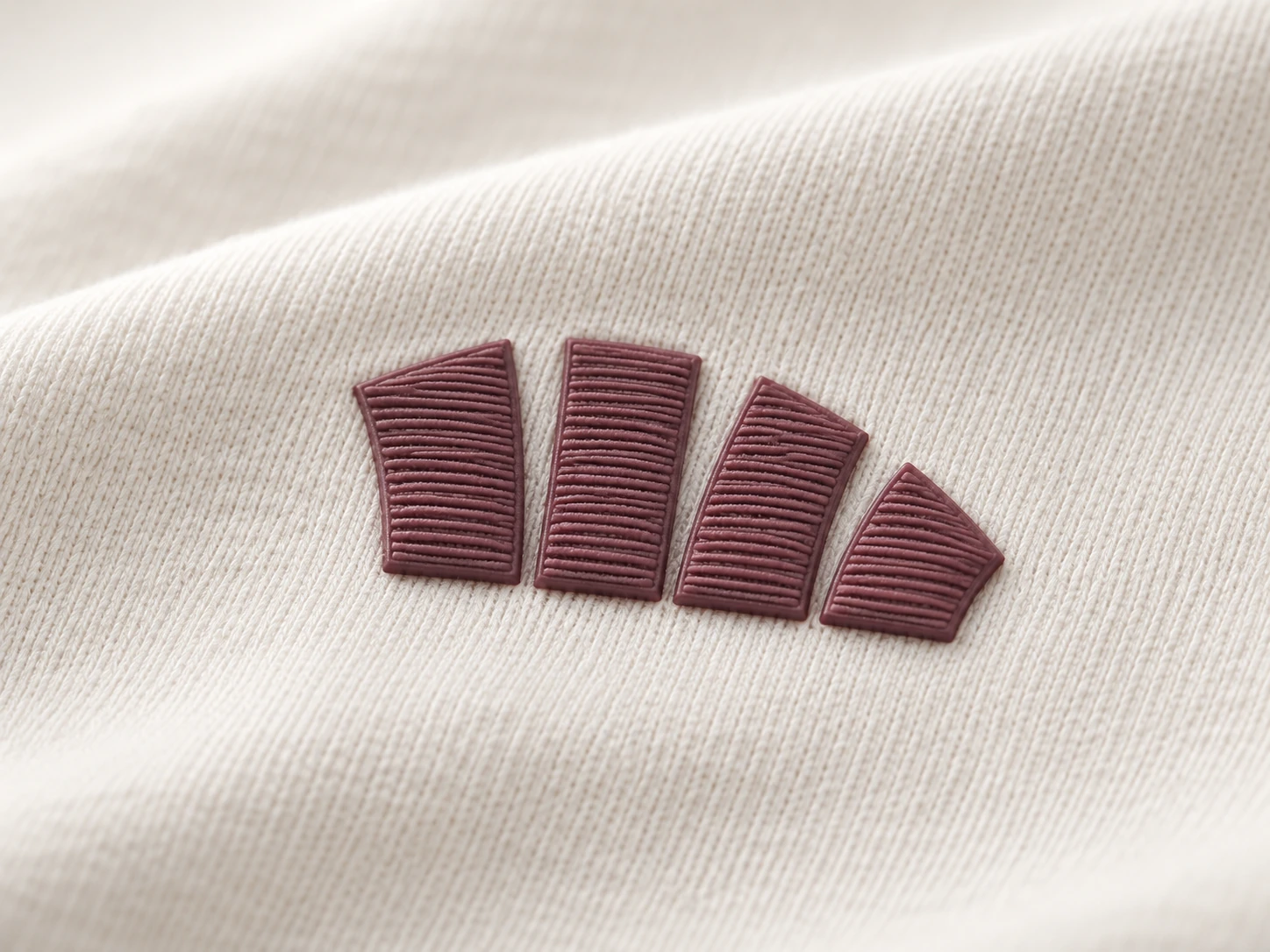 Four burgundy faux-embroidery silicone transfer shapes on ivory knit.